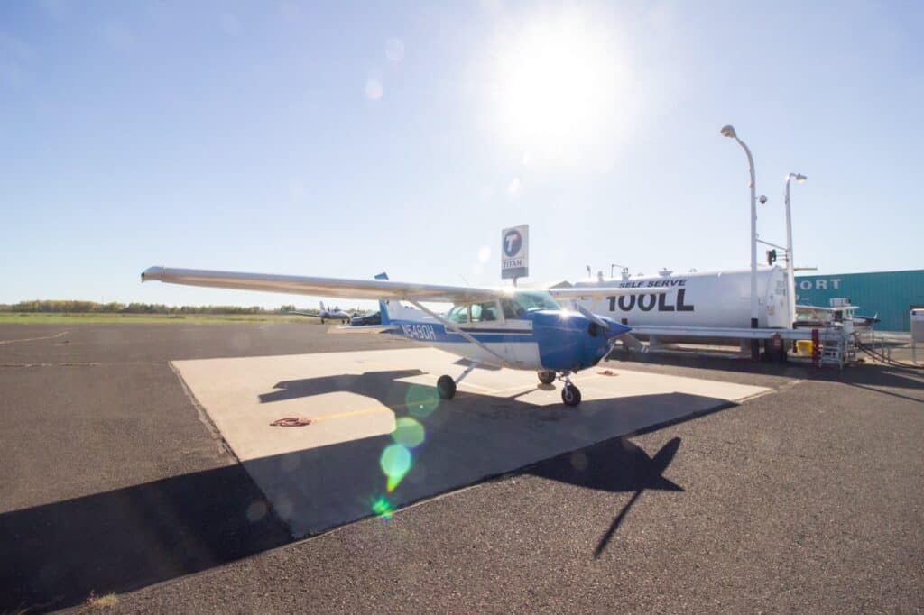 The blue-and-white Cessna 172M N5490H at the self-serve 100LL pump at KSUW.