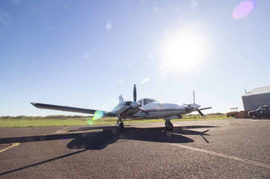 The twin-engine Piper Seneca on the ramp at KSUW, seen head-on with the sun behind it.
