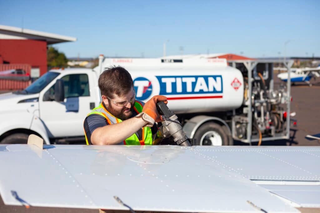 A Superior Flying Services line technician in a hi-vis vest fuelling an aircraft wing from the Titan Aviation Fuel truck.