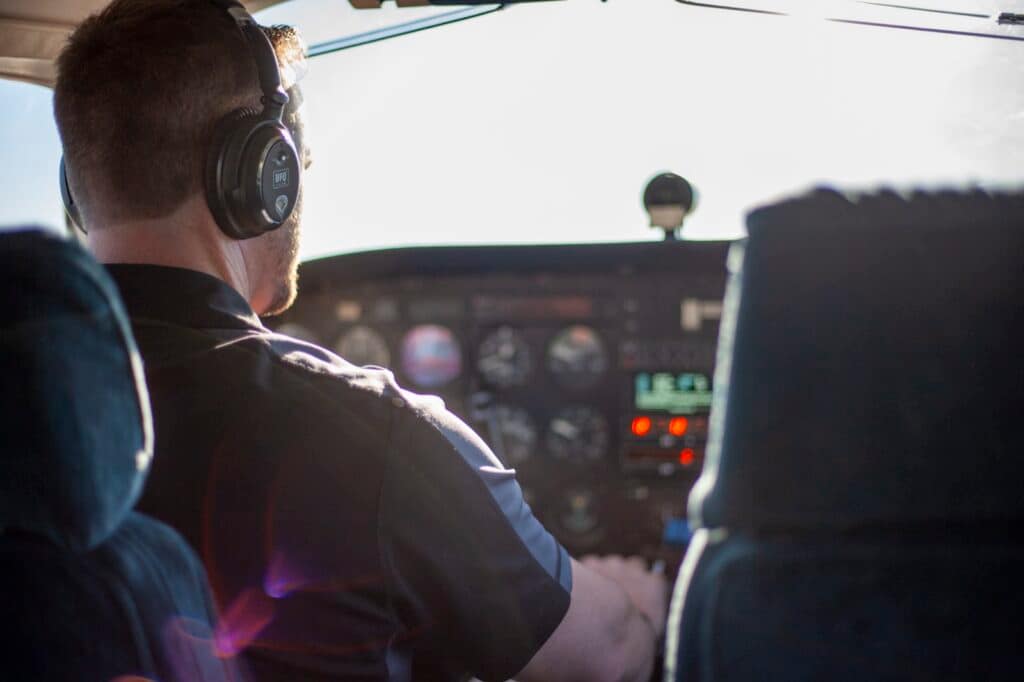A pilot in a headset flying from the left seat of a training aircraft, hands on the yoke, the instrument panel lit ahead of him.