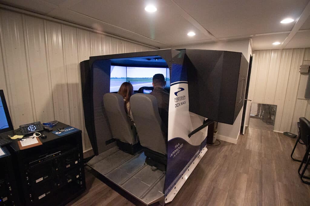 Two people flying the PFC DCX Max training device in the simulator room at Superior Flying Services.